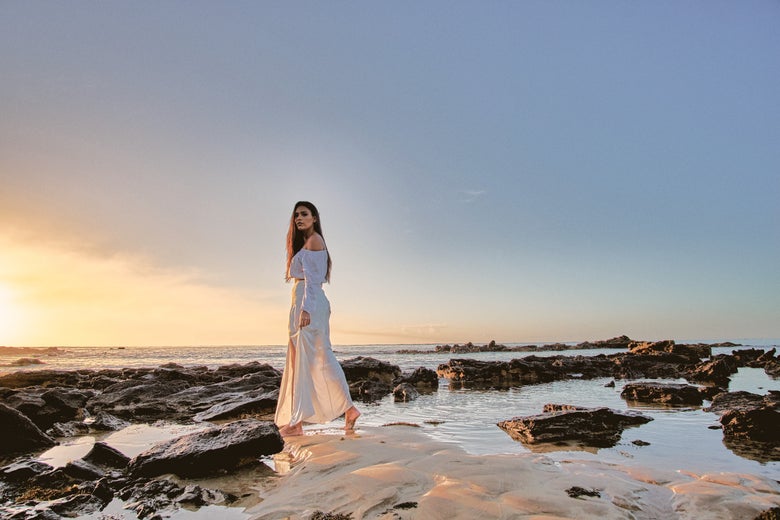 A woman in a white dress walks through a creek.
